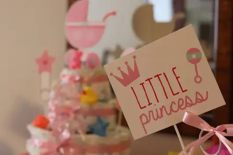 Urocza dekoracja na baby shower z napisem "Little princess", koroną i grzechotką. W tle tort z pieluch i różowa karoca. Prawdziwy mały **gwiazdor**!