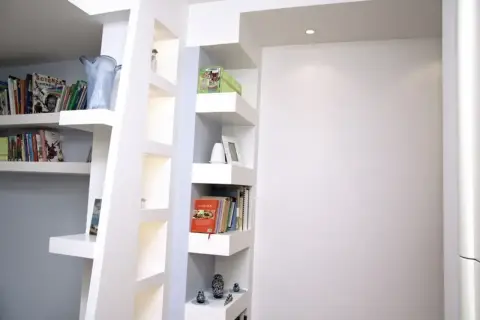 Scaffali moderni in cartongesso, con libri, vasi e soprammobili, creano un angolo lettura accogliente.