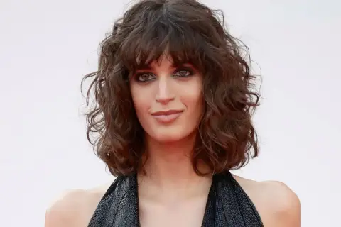 Mujer con curly pelo corto rizado natural, mirada intensa y vestido negro brillante.