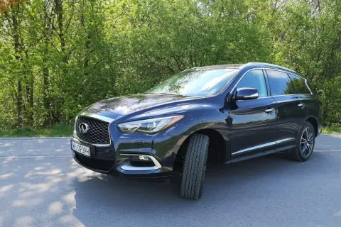 Ciemny Infiniti QX60 zaparkowany na poboczu drogi, otoczony zielenią drzew.