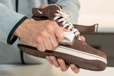 Man limpiando zapatillas de ante marrón con un cepillo blanco. Paso a paso para saber como limpiar zapatillas de ante y dejarlas como nuevas.