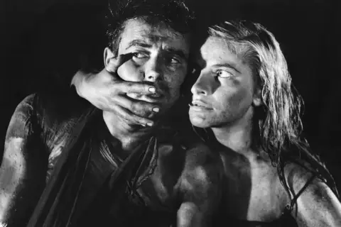 Dramatyczna scena z filmu Andrzeja Wajdy. Kobieta zakrywa usta mężczyźnie, ich twarze są spocone i brudne.