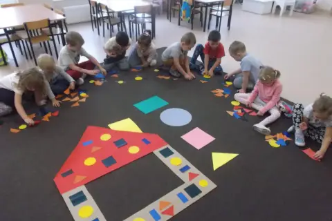 Dzieci w przedszkolu tworzą obrazki z kolorowych figur geometrycznych.
