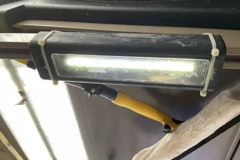 Jasne, oto opis:

Oświetlenie garażu bez prądu: prowizoryczna lampa LED na opaskach zaciskowych, oświetlająca wnętrze. Obok wisi narzędzie do czyszczenia.