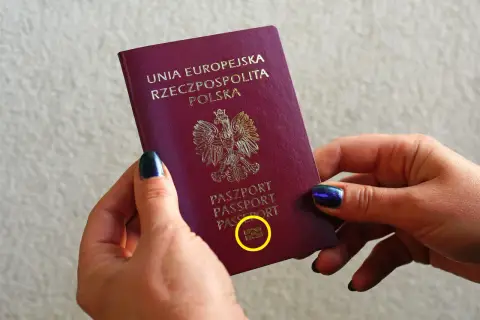 Dłonie trzymają polski paszport biometryczny z symbolem aparatu.