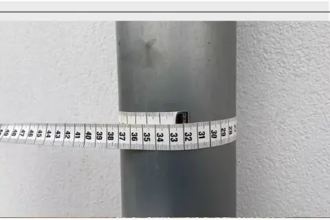 Miarka krawiecka owinięta wokół rury, pokazująca jej obwód. Odczyt wskazuje na średnicę około 32 cm.