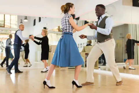 Coppia balla swing in una scuola di ballo. Altri ballerini si esercitano nello specchio.