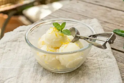 Un délicieux sorbet citron sans sorbetière, garni de menthe fraîche et de zestes de citron, servi dans un bol en verre.