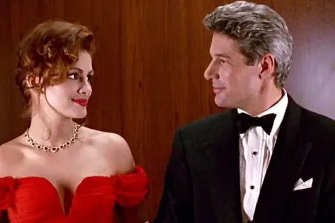 Para, która ogląda filmy dla par, w eleganckich strojach, kobieta w czerwonej sukni, mężczyzna w smokingu.