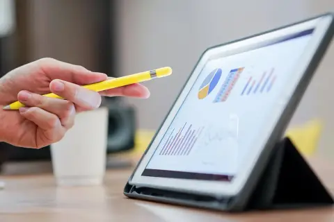 Dłoń z żółtym rysikiem wskazuje na wykresy na tablecie. Analiza danych, być może dotyczących hipoteki odwróconej, w biurze.