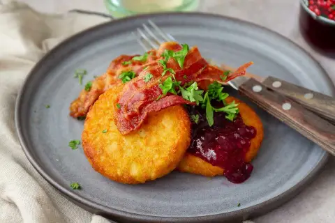 Gylla potatisbullar airfryer med knaprigt bacon, lingonsylt och persilja på en grå tallrik. En klassisk svensk rätt.
