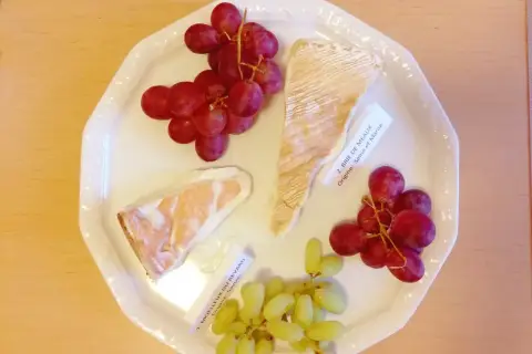 Talerz z serami Brie de Meaux i Moelleux du Revard, winogronami i etykietami, idealny do degustacji kuchni francuskiej.