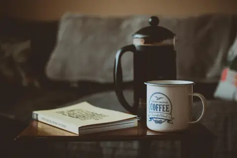 French press z kawą, kubek z napisem "Coffee" i książka o kawie. Idealny zestaw, by dowiedzieć się, ile kawy do french press.