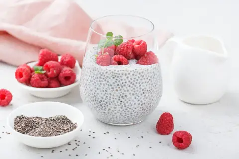 Pyszny deser chia pudding z malinami i miętą, obok miseczka z nasionami chia i świeżymi malinami.