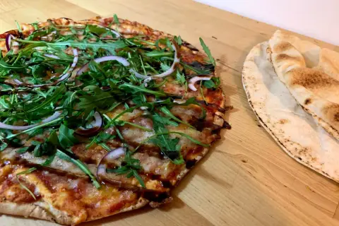 En läcker vegetarisk pizza med ruccola och rödlök, perfekt för dig som söker vegetariska recept. Bredvid ligger nybakade pitabröd.