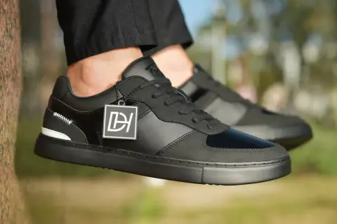 Baskets noires stylées, avec un jean qui détient sur la chaussure. Logo DH sur une étiquette.
