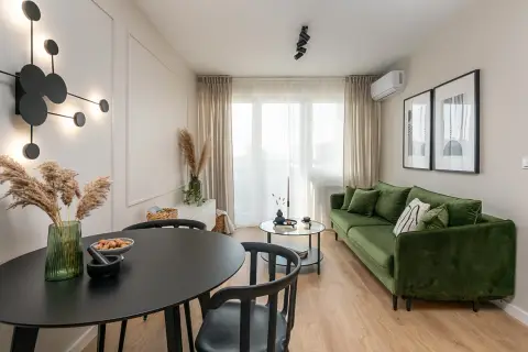 Nowoczesne mieszkanie w bloku z zieloną kanapą, czarnym stołem i designerską lampą.