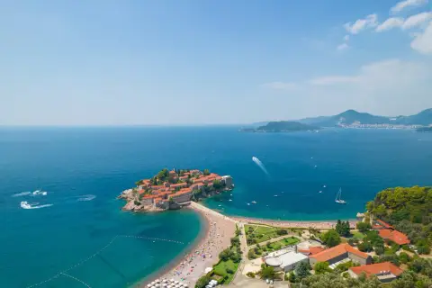 Idealne czarnogóra wakacje: wyspa Sveti Stefan z kamiennymi domkami i plażą pełną turystów, otoczona turkusowym morzem.