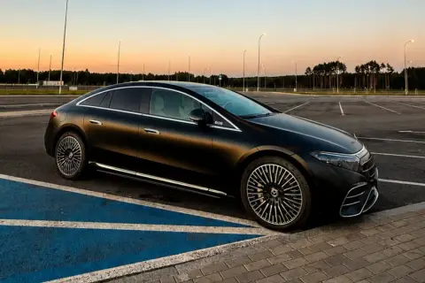 Elegancki, czarny Mercedes EQS na pustym parkingu o zachodzie słońca. Luksusowa limuzyna elektryczna prezentuje swoje aerodynamiczne linie.