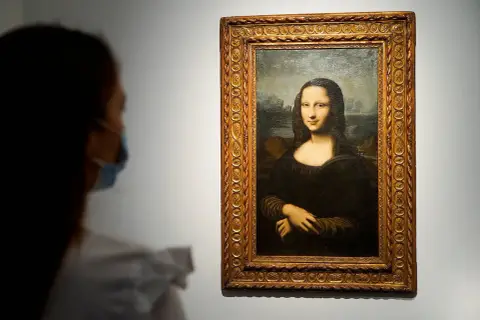 Eine Person mit Maske betrachtet die Mona Lisa. Ihre rätselhafte Bedeutung fasziniert seit Jahrhunderten.