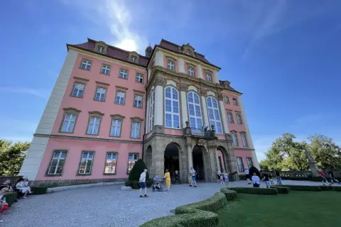 Zamek Książ, łatwy dojazd PKP, zachwyca różową fasadą i barokową architekturą. Turyści spacerują po brukowanym dziedzińcu.