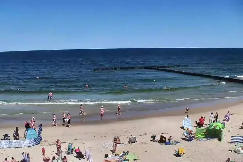 Słoneczna plaża w Dźwirzynie, ludzie kąpią się w morzu i odpoczywają na piasku. To jedne z wielu atrakcji tego miejsca.