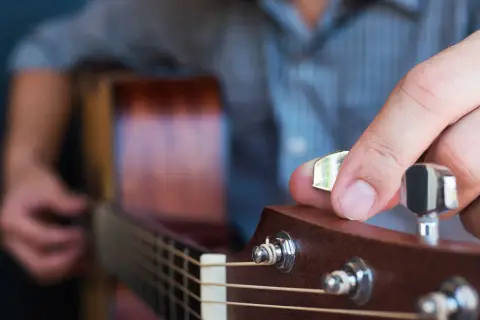Dłoń stroi gitarę klasyczną, obracając kluczem. Widać struny i fragment gryfu.