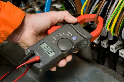 Elektryk mierzy spadek napięcia na przewodzie za pomocą cęgów mierniczych.