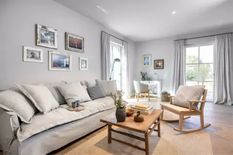 Gemütliches Wohnzimmer mit einem großen grauen Sofa, Bilderwand und Schaukelstuhl. Tolle wohnzimmer ideen graues sofa.