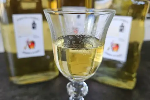 Szklanka z domową whisky "pudrową" z miodem i przyprawami, w tle butelki. Idealna na zimowe wieczory.