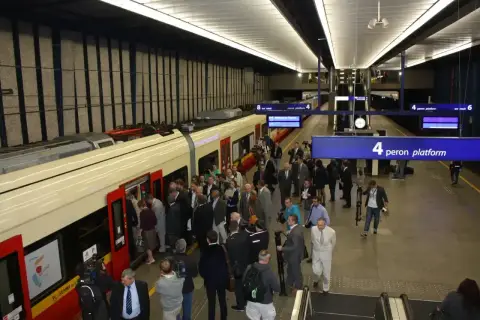 Ludzie wsiadają do pociągu na peronie 4. To część infrastruktury łączącej lotniska w Warszawie z centrum miasta.