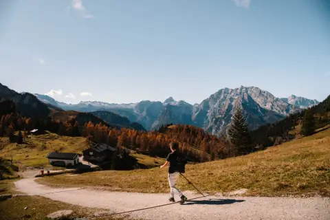 A lone hiker enjoys a scenic autumn day hiking in Bavaria, with colorful trees and majestic mountains in the background.