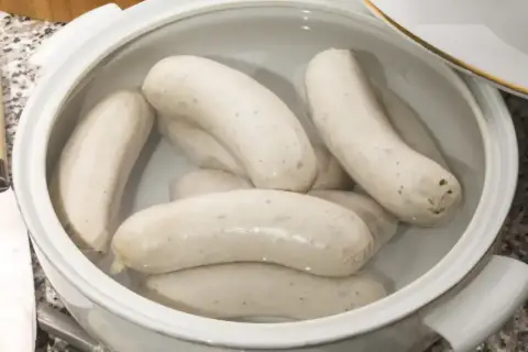 Kilka białych kiełbasek parzonych w garnku, gotowych do podania.