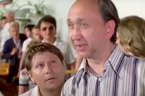Dwóch mało znanych aktorów polskich w kolejce. Jeden z nich, w pasiastym ubraniu, mówi coś do drugiego, który patrzy na niego z uwagą.