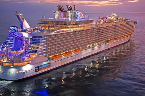Ogromny statek wycieczkowy Royal Caribbean lśni w blasku zachodzącego słońca, z kolorowymi światłami i zjeżdżalniami wodnymi.