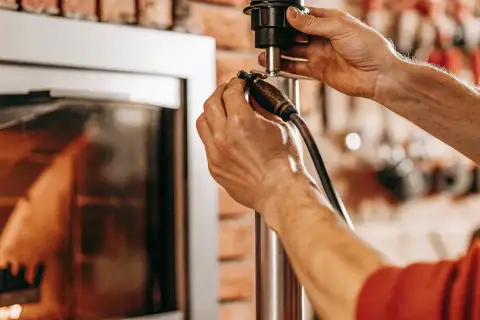 Ręce majsterkowicza przy piecu na ekogroszek. Zastanawiasz się, ile kosztuje wymiana ślimaka w piecu na ekogroszek?