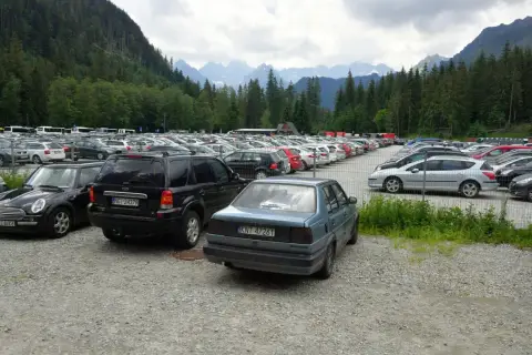 Duży parking samochodowy u podnóża gór, z widokiem na Tatry, jakby eic morskie oko patrzyło z góry.