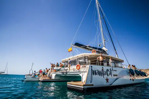 Catamarán "Juanita Cat" listo para el ferry Lanzarote La Graciosa. Turistas disfrutan del sol y el mar azul.