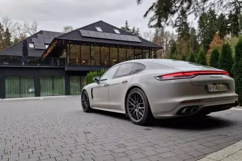 Białe Porsche Panamera GTS przed nowoczesnym budynkiem z panelami słonecznymi. Idealny wybór dla firm ceniących leasing operacyjny.