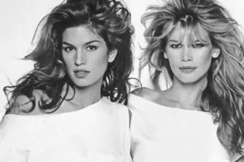 Dos icónicas modelos de los 90, Cindy Crawford y Claudia Schiffer, posan con sus melenas al viento y atuendos blancos.