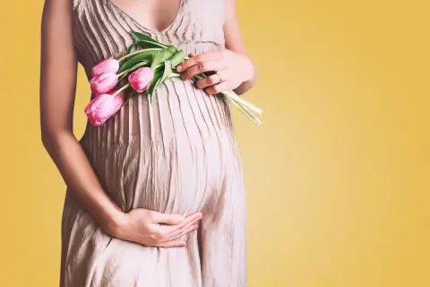 Kobieta w ciąży trzyma bukiet różowych tulipanów. Czas oczekiwania na dziecko to około 40 tygodni.