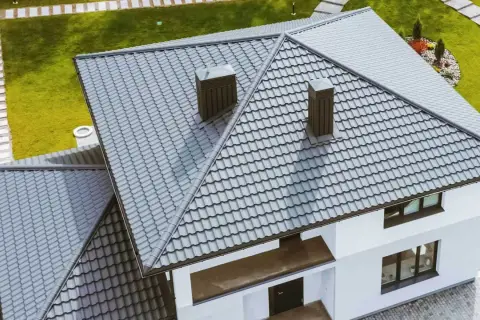 Nowy dom z szarym, nowoczesnym dachem dwuspadowym łamanym, z dwoma kominami i zielonym ogrodem.