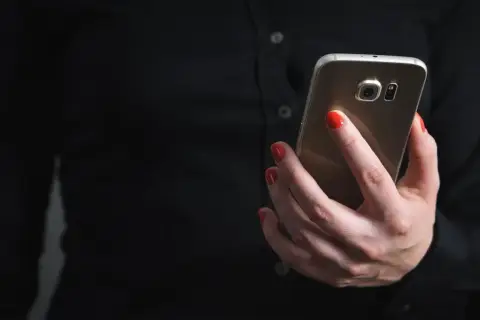 Dłoń z czerwonymi paznokciami trzyma telefon, szukając informacji, jak zablokować SMS premium.