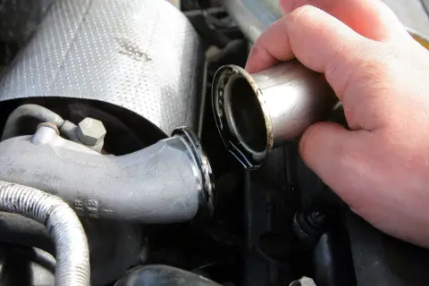 Dłoń trzymająca metalową rurkę z widocznymi śladami oleju, część układu dolotowego turbiny auto.