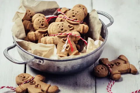Un cuenco lleno de galletas de jengibre con forma de hombrecito, algunas atadas con hilo rojo y blanco.