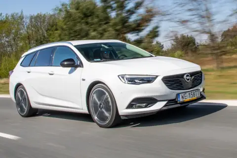 Białe kombi Opel Insignia 2.0 CDTI pędzi po drodze, za kierownicą mężczyzna w okularach przeciwsłonecznych.