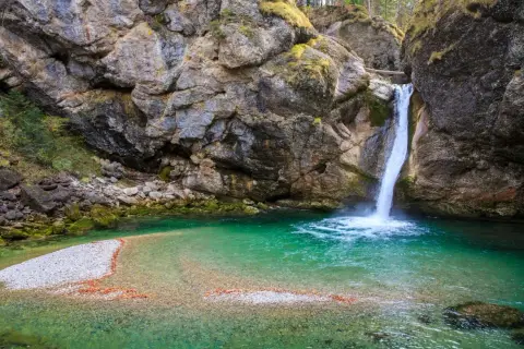 Türkiser bergsee mit einem tosenden wasserfall, der in die klare Tiefe stürzt. Felsen und Moos umrahmen dieses Naturschauspiel.