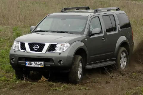 Szary Nissan Pathfinder r51 pokonuje błotniste wzniesienie, wzbijając tumany kurzu.