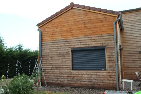 Échelle près d'un mur en bois, suggérant un entretien du bardage bois. Le bois est plus clair en haut, plus foncé en bas.