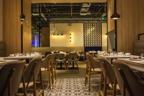 Przytulne wnętrze restauracji z drewnianymi panelami i stylowym oświetleniem. Stoliki nakryte, gotowe na gości.